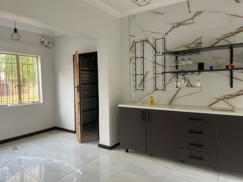 A modern, minimalist bar area featuring dark built-in cabinetry, a stone countertop, and elegant marble-effect wall tiling with integrated shelving.