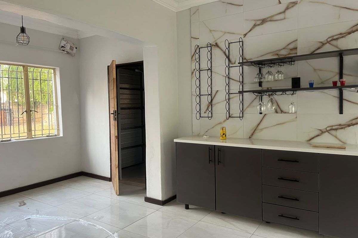 A modern, minimalist bar area featuring dark built-in cabinetry, a stone countertop, and elegant marble-effect wall tiling with integrated shelving.