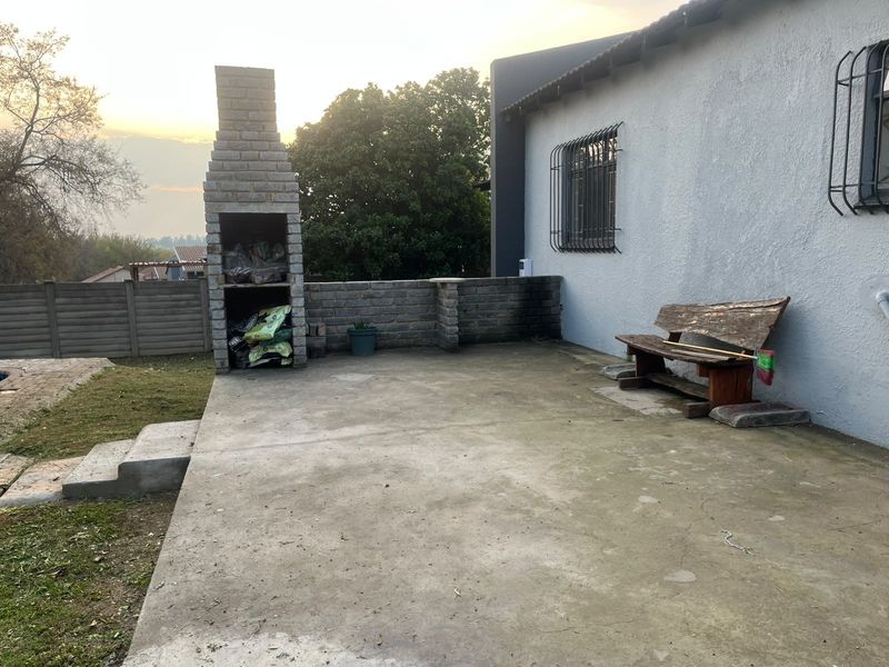 Outdoor patio area featuring a built-in brick braai, concrete flooring, and security bars on the windows, offering potential for an upgraded entertainment space.