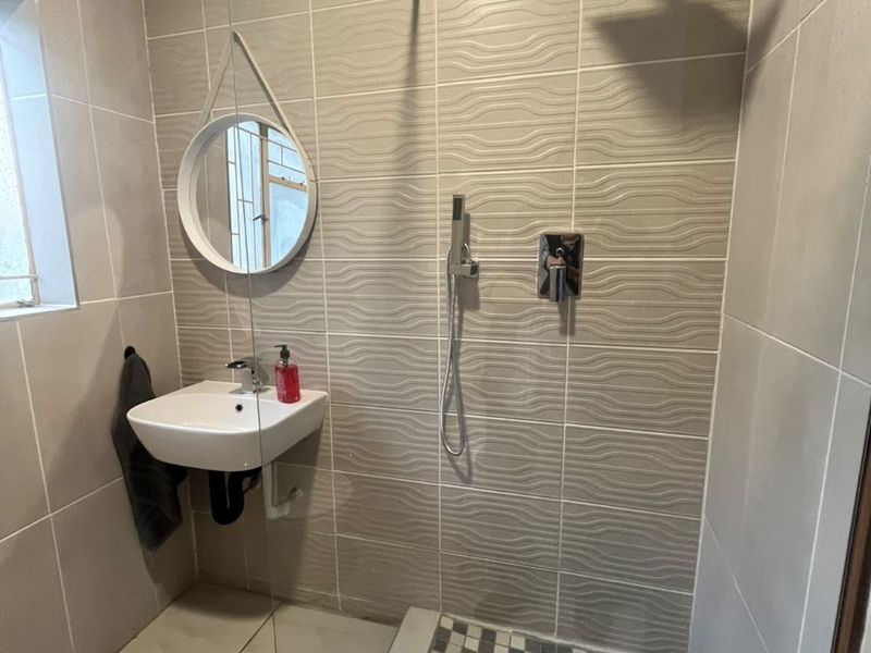 Modern bathroom featuring a walk-in shower with a rain shower head, textured wall tiling, and a wall-mounted basin.