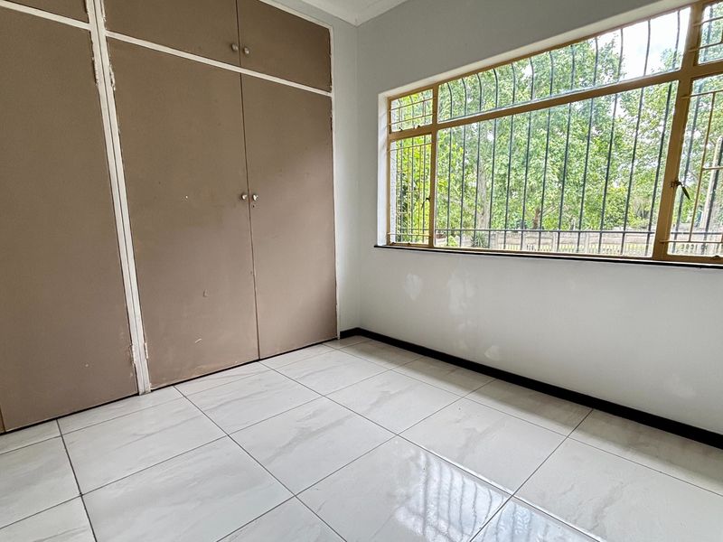 A bright, empty bedroom featuring tiled flooring, built-in cupboards, and large windows with security bars, offering a clean canvas for personalization.