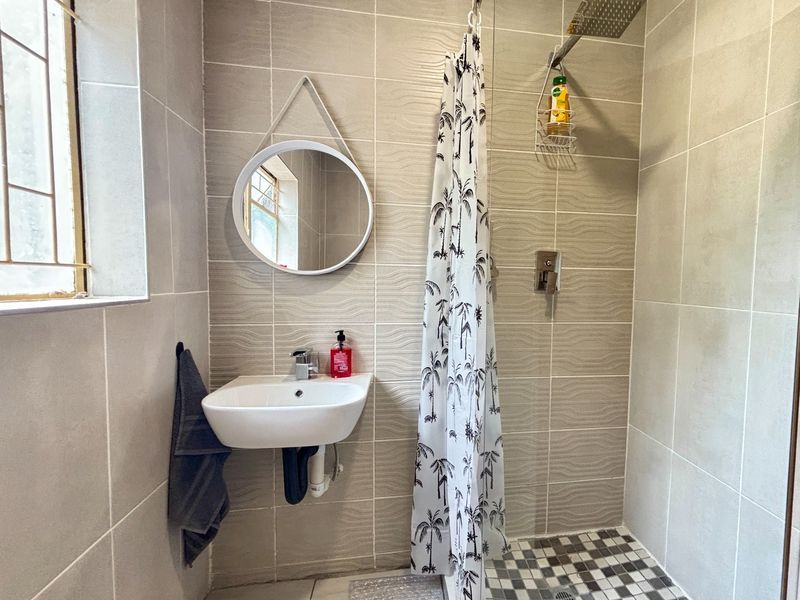 Compact bathroom featuring a wall-mounted basin, tiled shower area with a rainfall shower head, and neutral wall tiling.