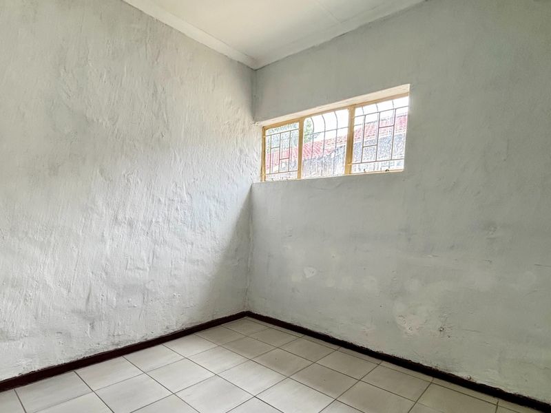 An empty bedroom featuring tiled flooring, security bars on the window, and walls requiring cosmetic attention and repainting.