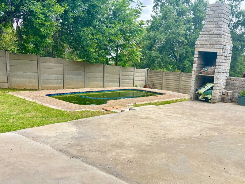 Outdoor pool area featuring a concrete patio, built-in brick braai, and a swimming pool requiring maintenance, enclosed by a precast boundary wall.
