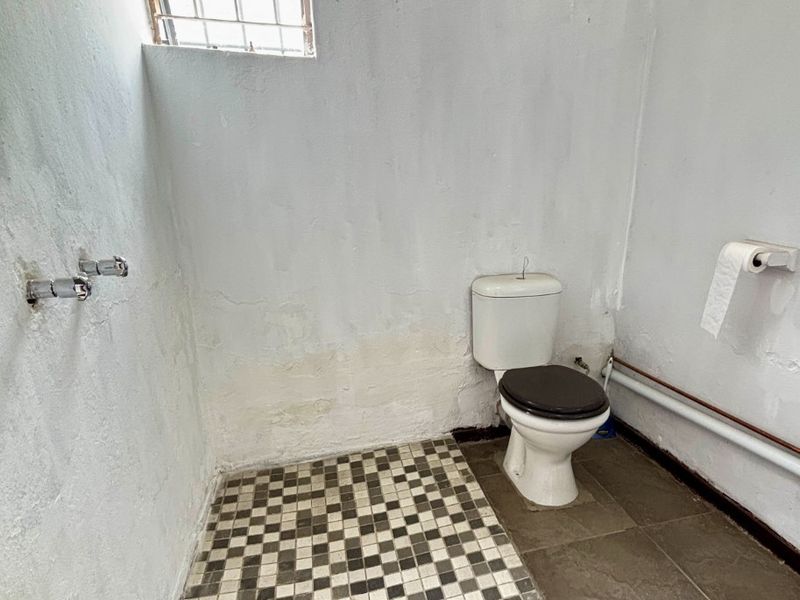 A basic bathroom featuring a toilet, shower area with floor drain, and security window. The space requires cosmetic renovation and wall repairs.