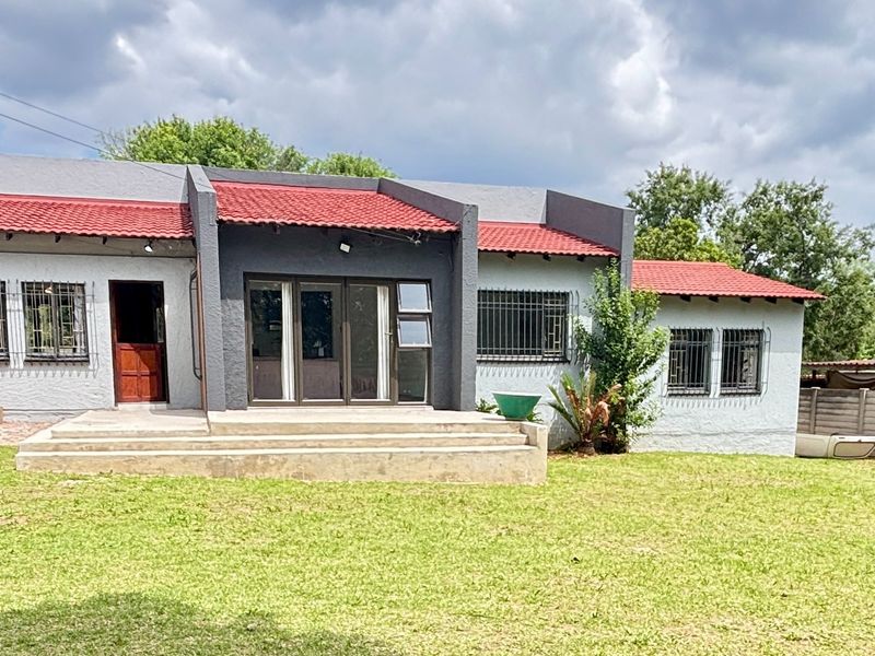 Rear view of the house featuring a red tiled roof, concrete patio, and secure window bars overlooking a spacious lawn.