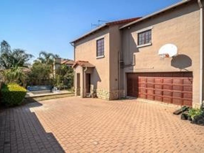 Rear view of the property featuring a paved driveway, double garage, and a swimming pool set within a landscaped garden area.