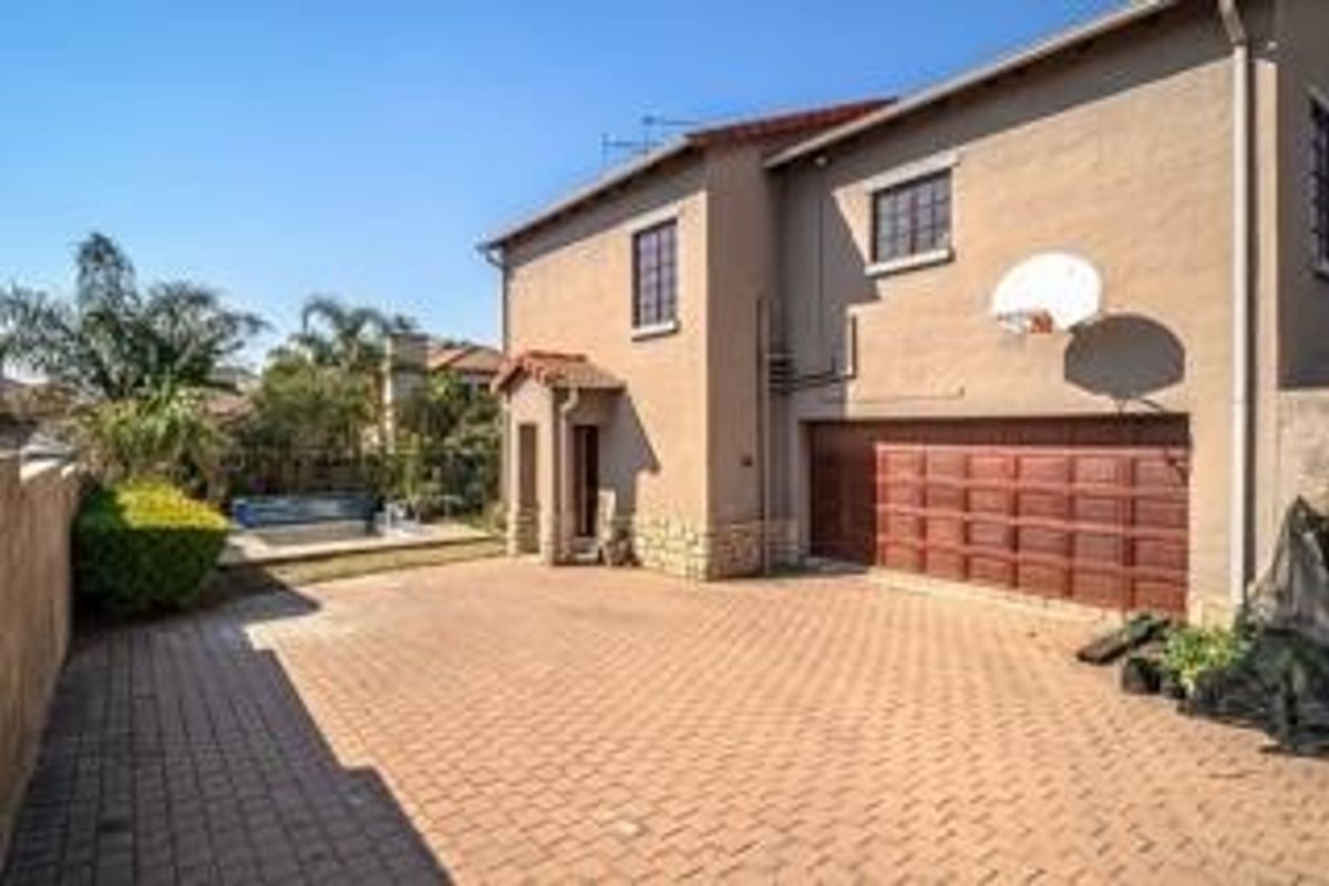 Rear view of the property featuring a paved driveway, double garage, and a swimming pool set within a landscaped garden area.