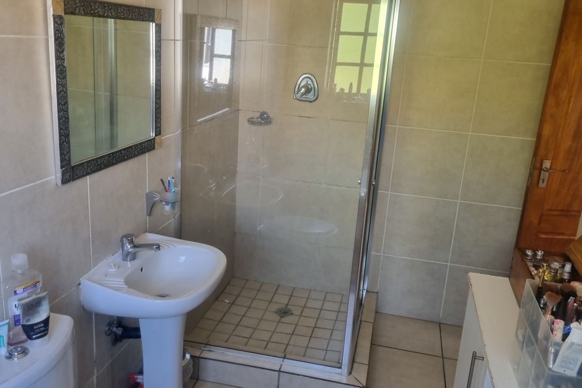 A functional bathroom featuring a pedestal basin, a glass-enclosed shower, and neutral wall and floor tiling.