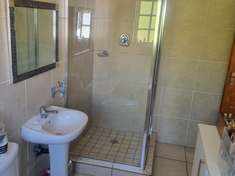 A functional bathroom featuring a pedestal basin, a glass-enclosed shower, and neutral wall and floor tiling.