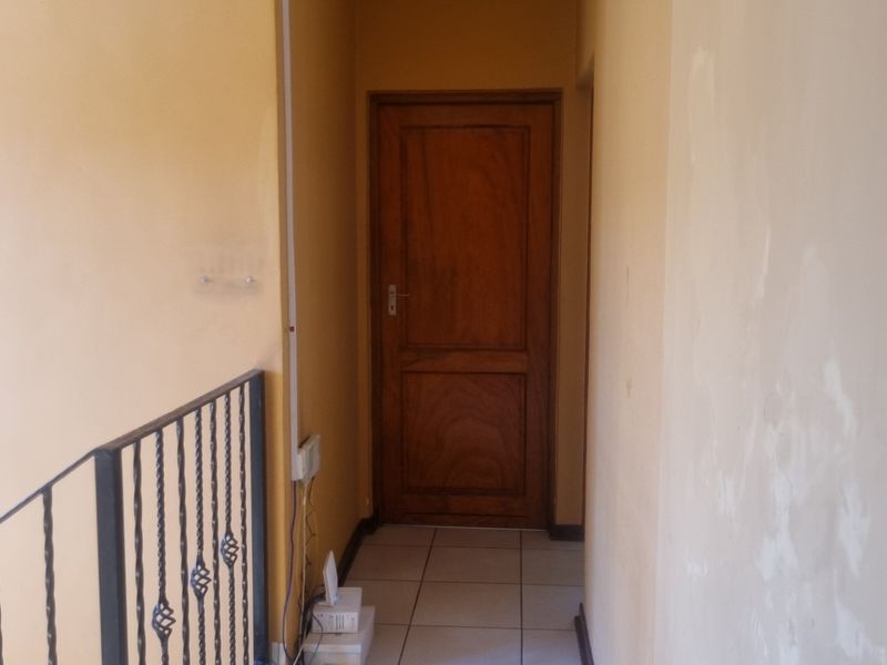 A narrow hallway featuring tiled flooring, a wrought iron balustrade, and a timber door, currently showing signs of wall surface wear and peeling paint.