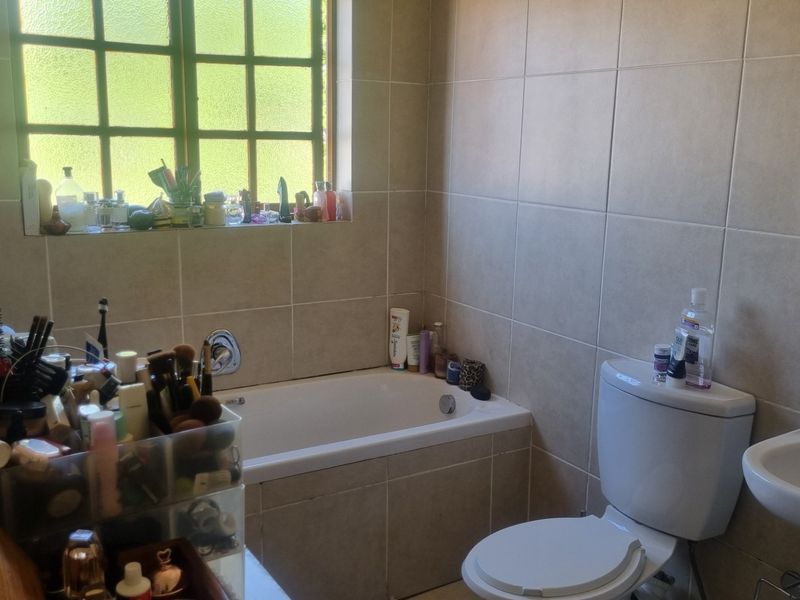 A functional bathroom featuring a built-in bathtub, pedestal washbasin, and neutral ceramic wall tiling with a grid-pattern window for natural light.