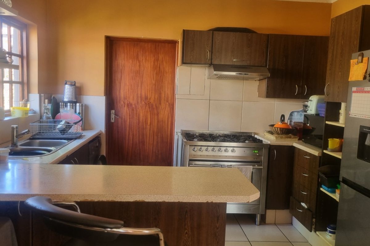 A functional kitchen featuring dark wood cabinetry, a stainless steel gas stove with extractor fan, tiled backsplash, and a convenient breakfast counter.