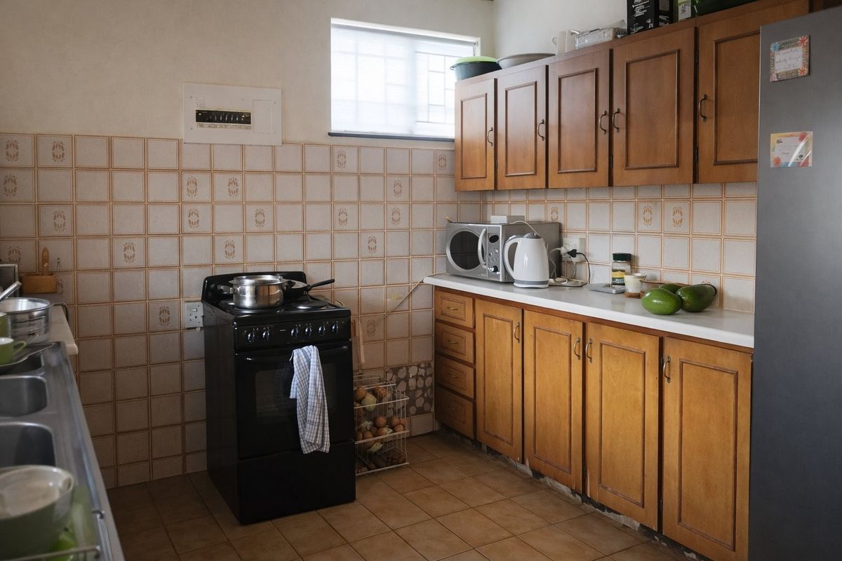 A functional kitchen featuring wooden cabinetry, a freestanding stove, double sink, and tiled finishes, offering potential for a modern renovation.