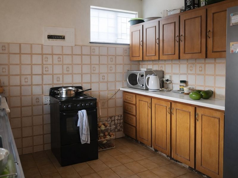 A functional kitchen featuring wooden cabinetry, a freestanding stove, double sink, and tiled finishes, offering potential for a modern renovation.