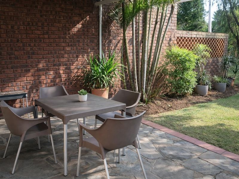 A covered outdoor patio area featuring stone paving and an exposed brick wall, overlooking a landscaped garden with a decorative brick screen.