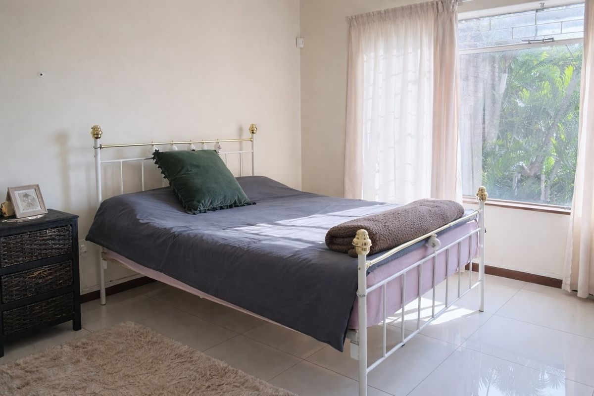 A bright bedroom featuring neutral tiled flooring and a large window allowing for natural light.