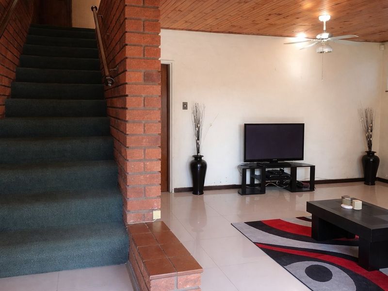 Living room featuring exposed brick staircase, timber ceiling, and tiled flooring, offering a dated aesthetic with potential for modernization.
