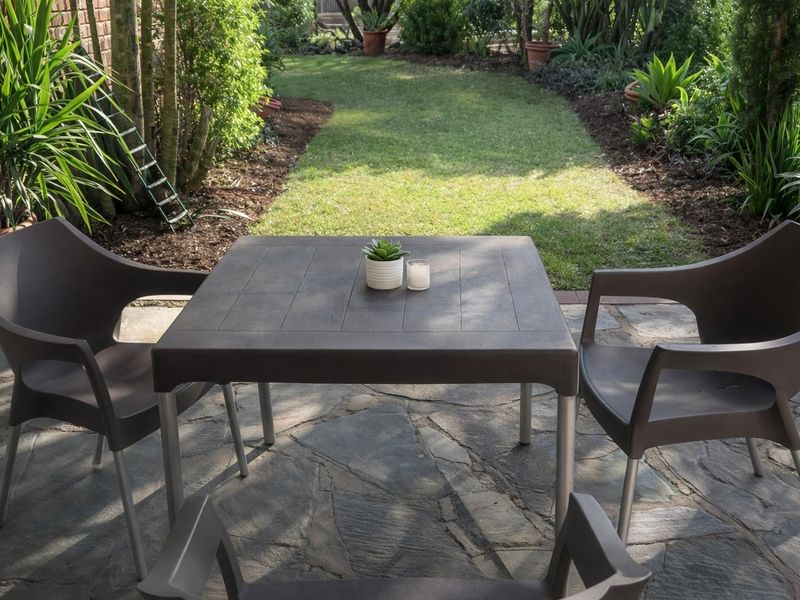 A paved outdoor patio area featuring natural stone flooring and a brick wall, overlooking a well-maintained garden space.
