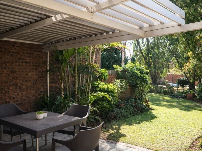 A covered outdoor patio area featuring brick wall finishes and paved flooring, overlooking a lush private garden.