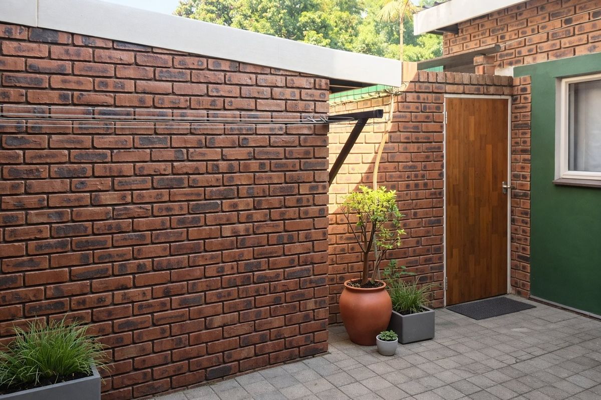 A private rear courtyard featuring face brick walls, paved flooring, and a wall-mounted clothesline, providing a functional outdoor utility space.
