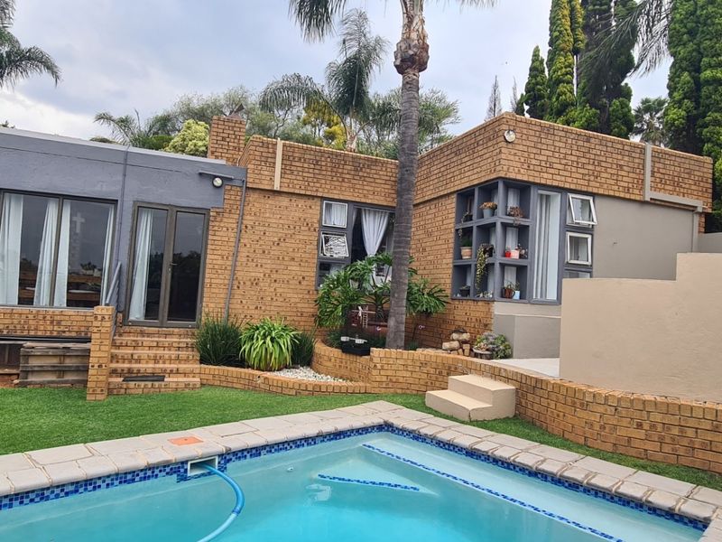 Rear exterior view featuring a swimming pool, brick facade, and landscaped garden area with tiered retaining walls.