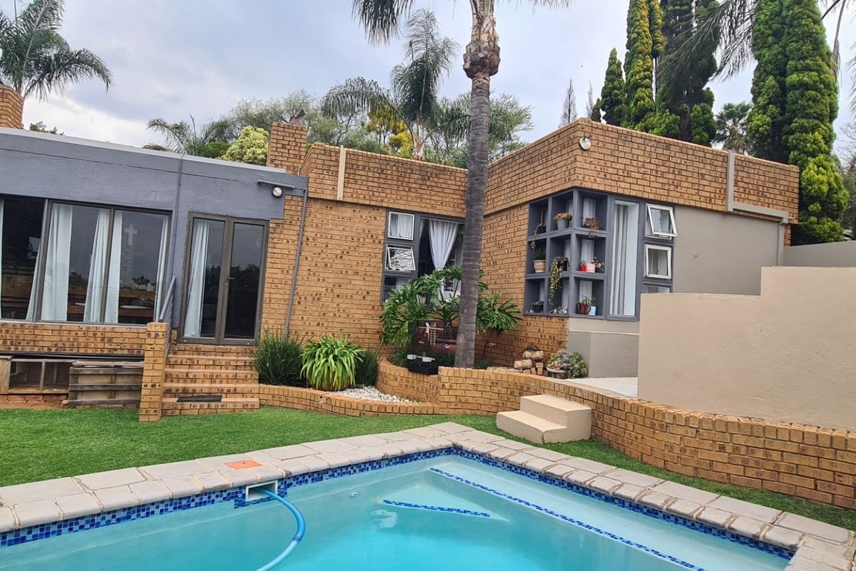 Rear exterior view featuring a swimming pool, brick facade, and landscaped garden area with tiered retaining walls.