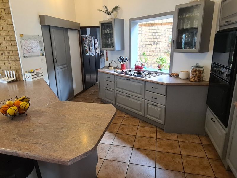 A well-maintained kitchen featuring grey cabinetry, a gas hob, built-in oven, and a spacious island with tiled flooring and an exposed brick feature wall.