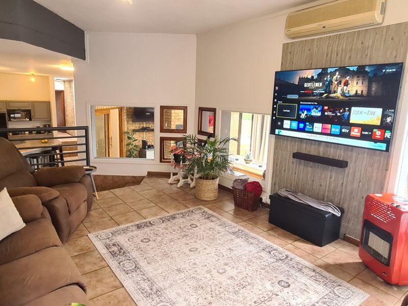 Spacious living room featuring tiled flooring, a brick feature wall, and a dedicated media wall panel with integrated air conditioning.