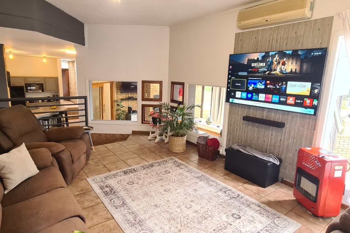 Spacious living room featuring tiled flooring, a brick feature wall, and a dedicated media wall panel with integrated air conditioning.