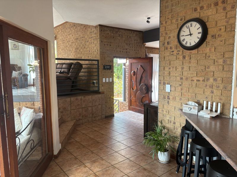 Entrance hall featuring exposed brick walls, tiled flooring, and a unique carved wooden front door, leading to a raised living area.