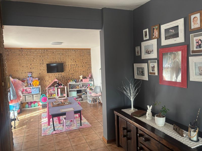 A living area featuring exposed brick walls and tiled flooring, currently utilized as a play space with an open-plan layout.