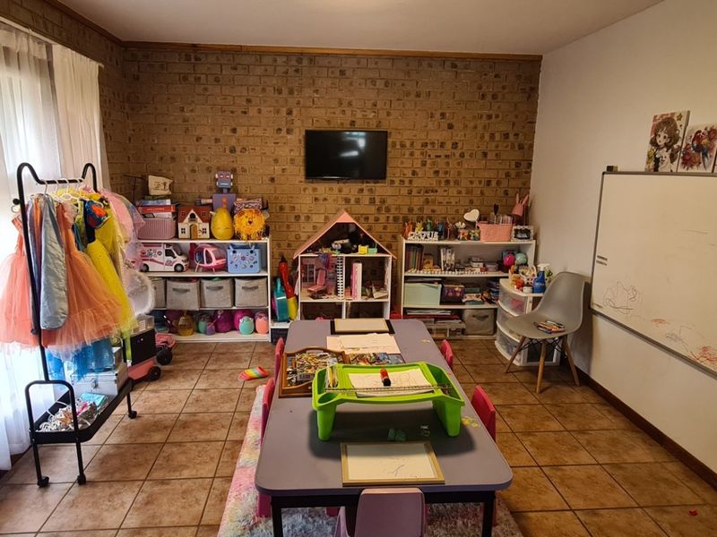 A living area featuring exposed brick walls and tiled flooring, currently utilized as a play and activity room with access to an outdoor area.