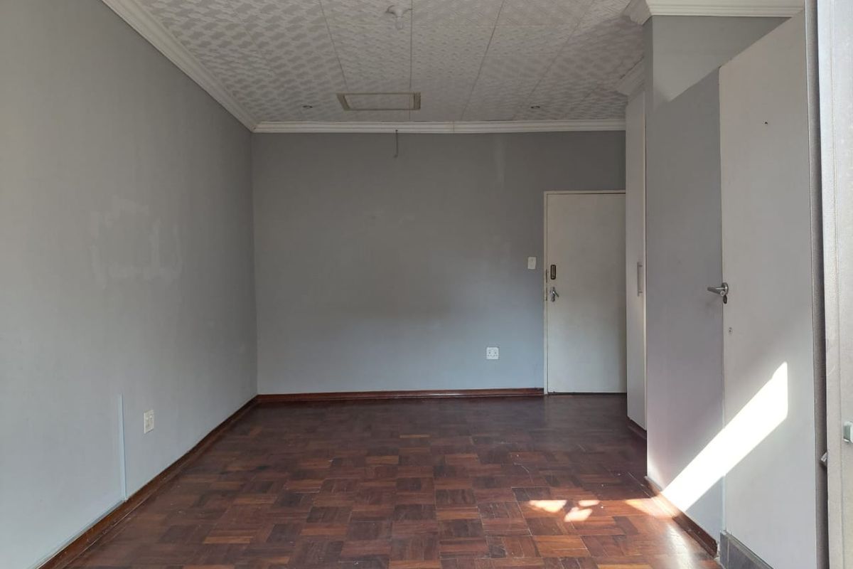 An empty bedroom featuring parquet flooring, built-in cupboards, and textured ceiling tiles, offering a blank canvas for personalization.
