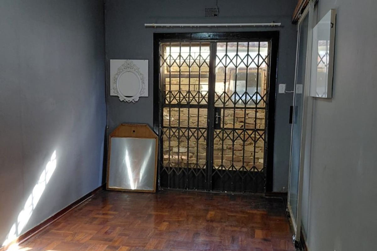An empty living area featuring classic parquet flooring, a sliding security gate, and decorative ceiling tiles, offering a blank canvas for interior design.