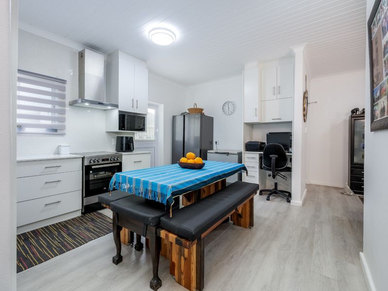 Modern kitchen featuring white cabinetry, stainless steel appliances, built-in oven, extractor fan, and integrated workspace area with light laminate flooring.