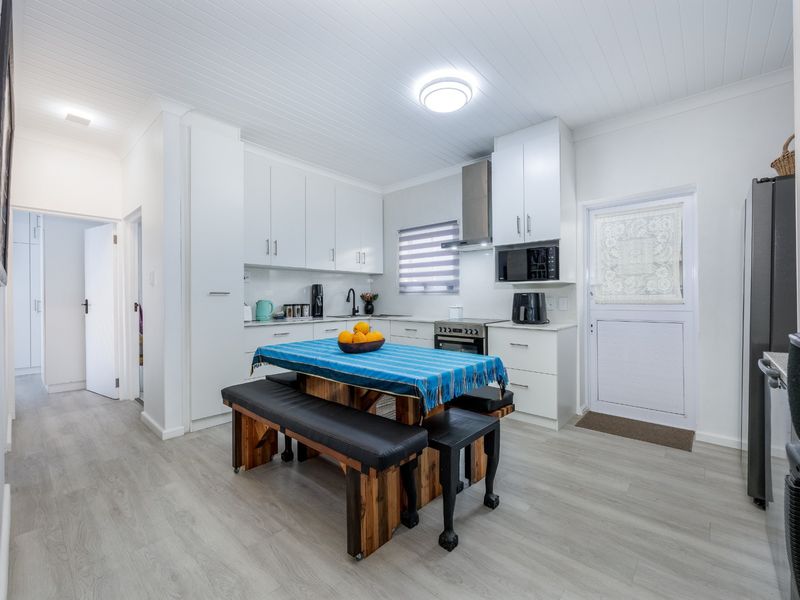 A bright, modern kitchen featuring white cabinetry, integrated appliances, laminate flooring, and a tongue and groove ceiling with direct access to the exterior.