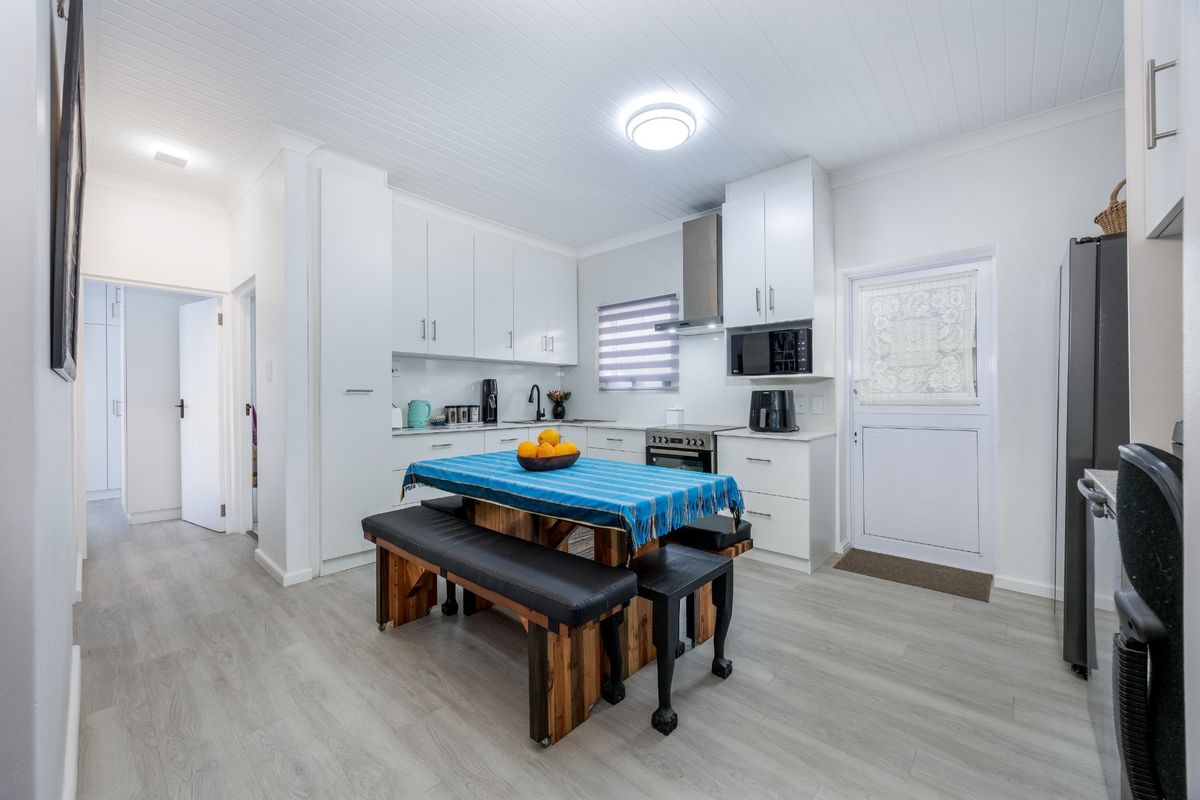 A bright, modern kitchen featuring white cabinetry, integrated appliances, laminate flooring, and a tongue and groove ceiling with direct access to the exterior.