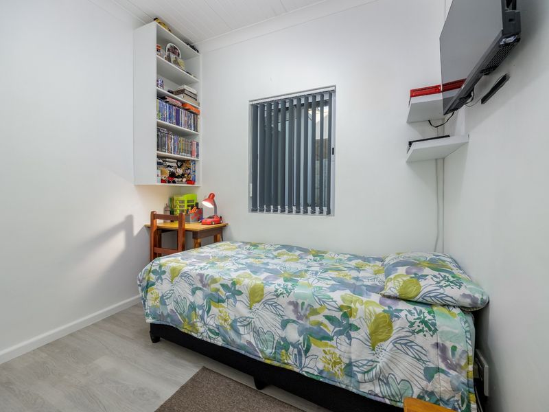 A compact bedroom featuring laminate flooring, built-in shelving, and vertical blinds, providing a functional and well-maintained living space.