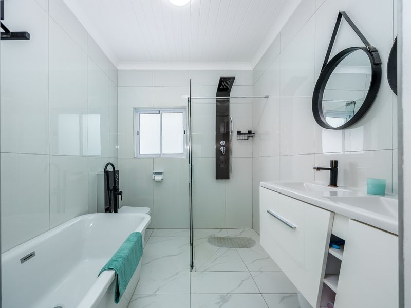 Modern bathroom featuring a sleek vanity, bathtub, and a glass-enclosed shower with a contemporary shower panel and high-quality tiled finishes.