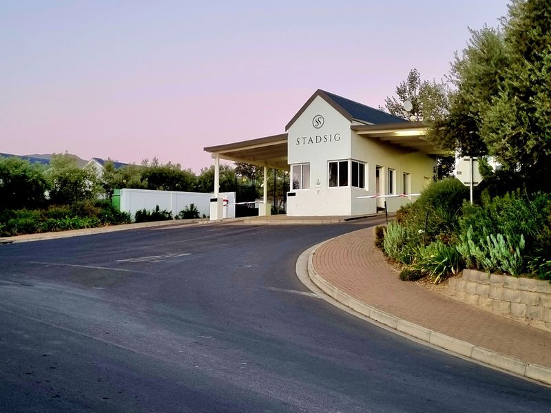 The entrance to Stadsig estate featuring a secure gatehouse, boom gate access, and well-maintained paved and asphalt driveway infrastructure.
