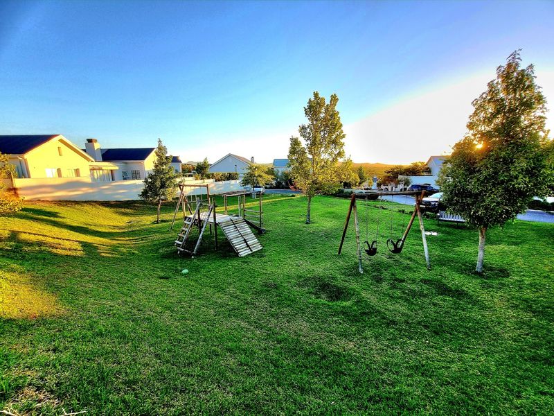 A spacious, well-maintained residential garden featuring a large lawn area and integrated playground equipment, enclosed by a perimeter wall.