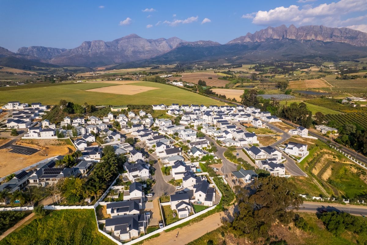 An aerial view of a residential estate featuring multiple detached homes with dark roofs, set against a scenic mountain landscape.