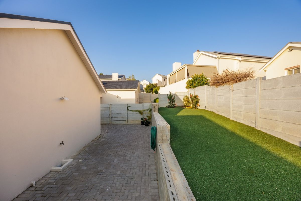 A low-maintenance rear garden featuring a paved walkway, artificial lawn, and secure precast concrete boundary walls.