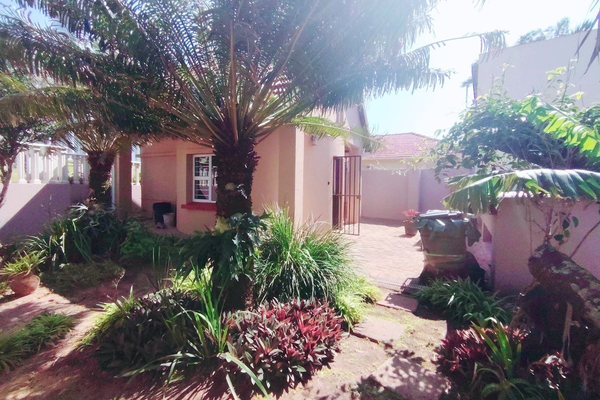 A rear garden area featuring a paved patio, established palm trees, and perimeter walling, providing a private outdoor space.