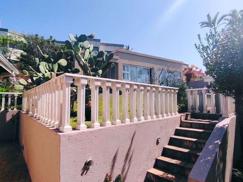 Rear exterior view featuring a raised terrace with a classic balustrade, concrete staircase, and paved ground level area.