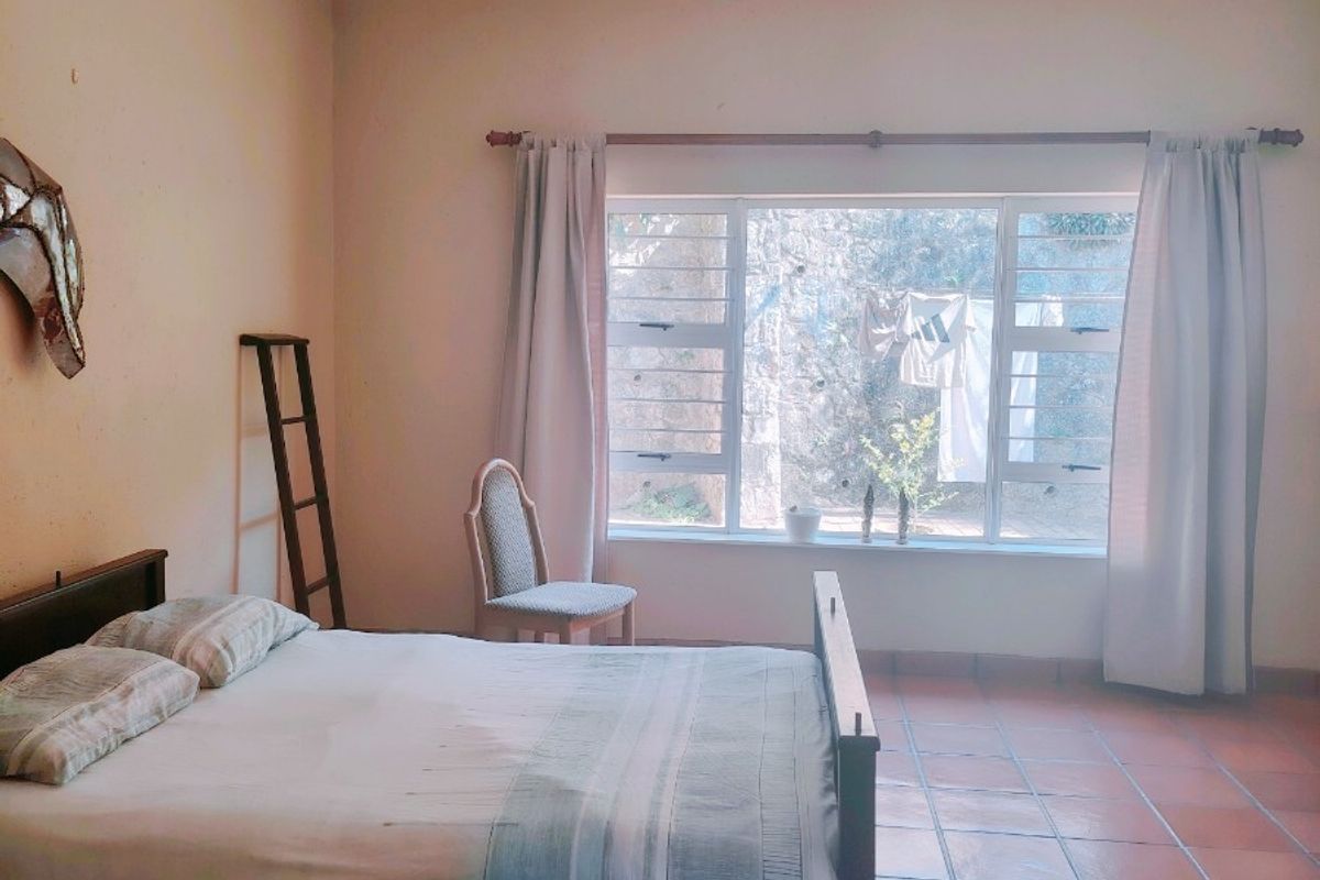 A spacious bedroom featuring terracotta floor tiles, a ceiling fan, and a large window allowing natural light.
