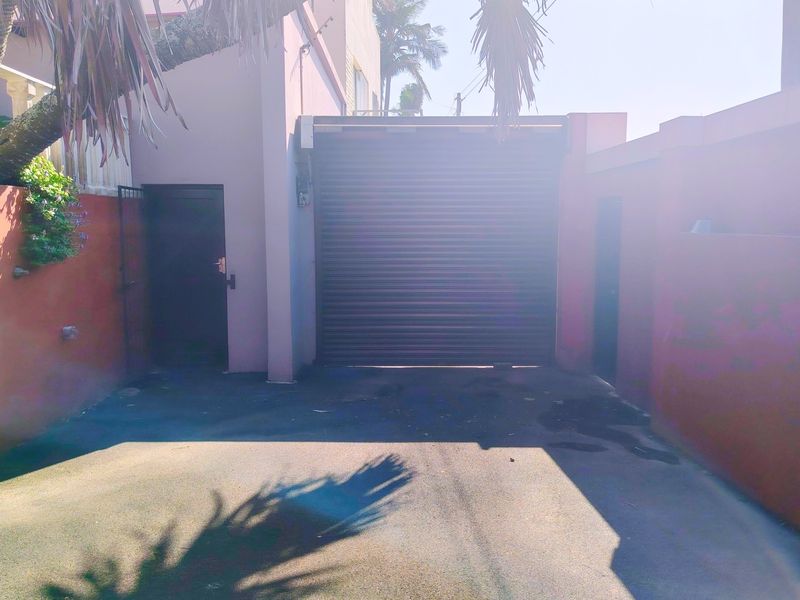 A private driveway leading to a secure garage with a roller shutter door, flanked by boundary walls and side access.