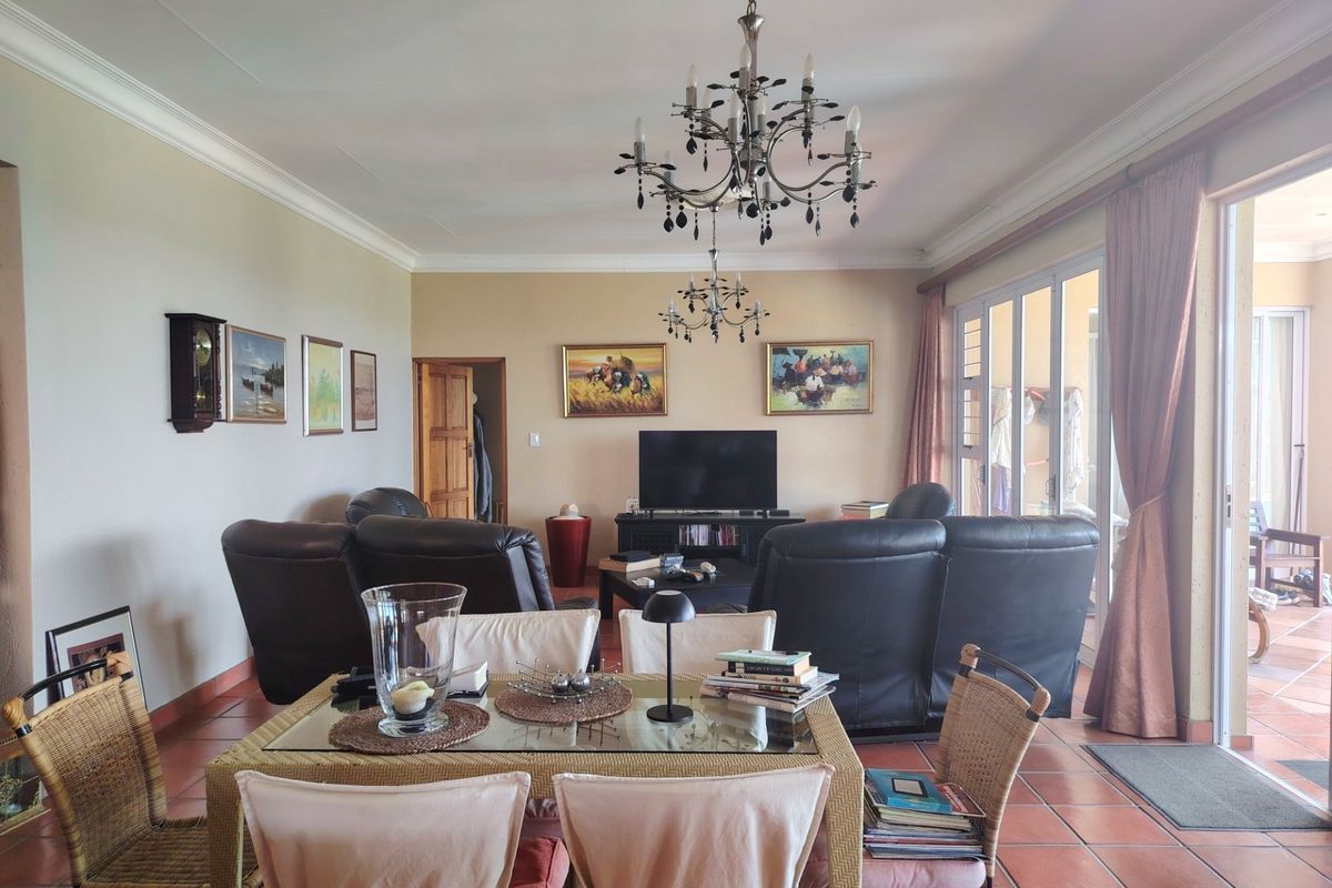 Spacious living area featuring terracotta floor tiles, decorative chandeliers, and large sliding glass doors providing access to the outdoor patio.