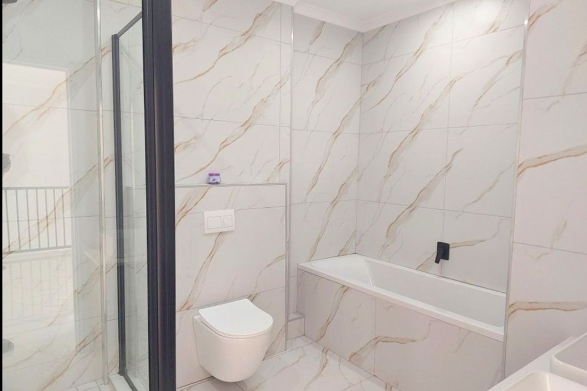 Modern bathroom featuring marble-look tiled walls and floors, a built-in bathtub, a wall-mounted toilet with concealed cistern, and a glass-enclosed shower.